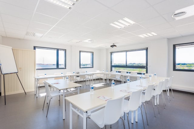 Salle de formation d'Espace Entreprise disposée en U avec paperboard, tables blanches et vue sur les collines
